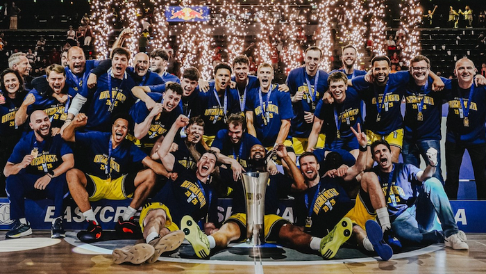 Begeistertes Basketballteam feiert Meisterschaftssieg mit Pokal und Medaillen auf dem Spielfeld.