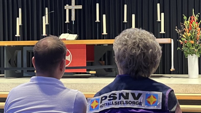 Eine Frau und ein Mann sitzen in einer Kirche und schauen auf dne Altar. Auf dem Rücken der Wester der Frau steht Notfallseelsorge.