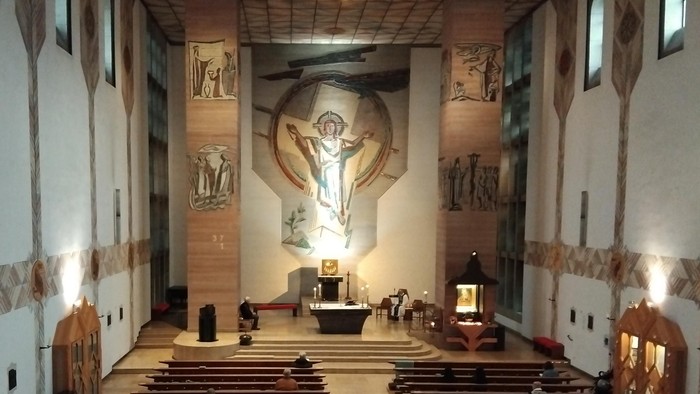 Modern gestaltete Kirche mit Holzpaneelen und großem Kreuz an der Wand