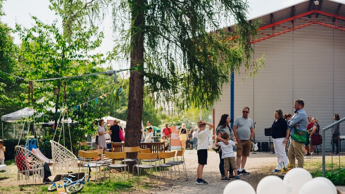 Draußen versammeln sich Menschen, die sich unterhalten, essen und Luftballons unter einem großen Baum genießen.