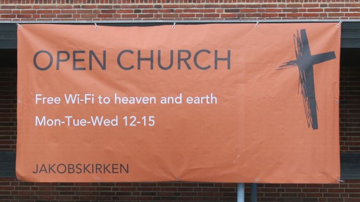 Rød banner med inviterende budskab til åben kirke med gratis Wi-Fi og åbningstider