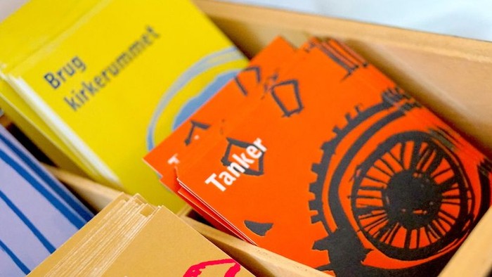 Farverige kassekort med tandhjul og mekaniske designs, mærket på dansk, pænt arrangeret i en træbakke.