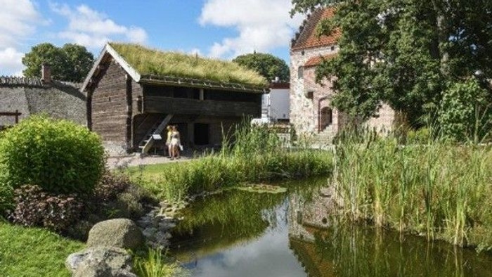 Charmerende historiske bygninger med græsklædte tage ved siden af en rolig, frodig vandvej.