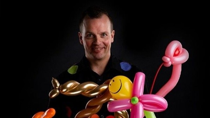 En mand holder kreativt en samling af farverige ballonfigurer og kreationer.