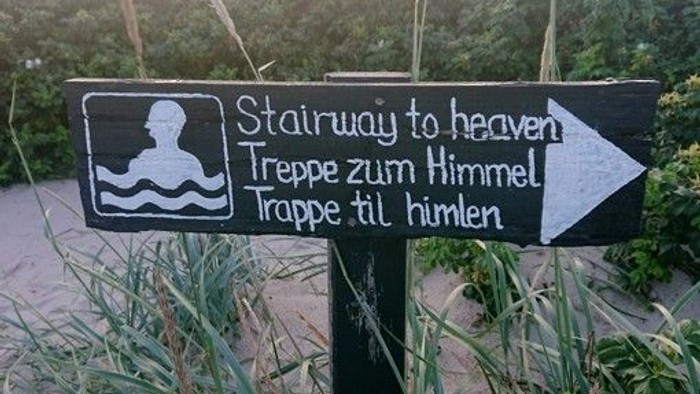 Ein verspieltes Schild mit der Aufschrift „Treppe zum Himmel“ mit Übersetzungen und einer Schwimmer-Grafik.