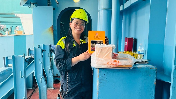 En person i sikkerhedsudstyr står stolt i et blåt industrielt køkkenområde og holder en sandwich.