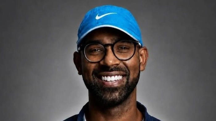 A picture of John Abraham wearing a running cap and smiling and holding the badge he was awarded for completing the challenge.