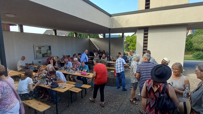 Gruppe von Menschen, die sich im Freien unter einem überdachten Pavillonbereich unterhalten und essen.