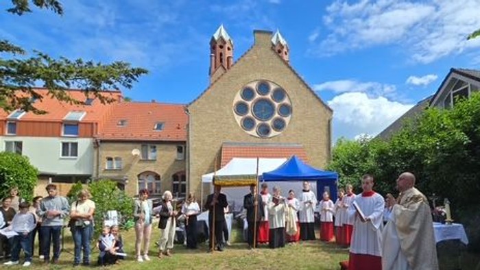 Draußen stattfindende religiöse Zeremonie mit Kindern und Geistlichen in weißen Gewändern, versammelt nahe einem Kirchengebäude.