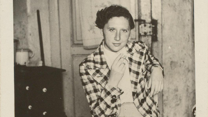 Eine Frau in kariertem Hemd und Rock sitzt nachdenklich auf einem Stuhl in einem vintage Zimmer.