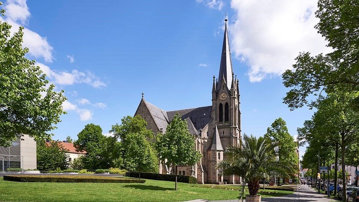 Eine friedvolle Kirche mit hohem Turm erhebt sich an einem strahlend sonnigen Tag inmitten eines üppigen, grünen Parks.