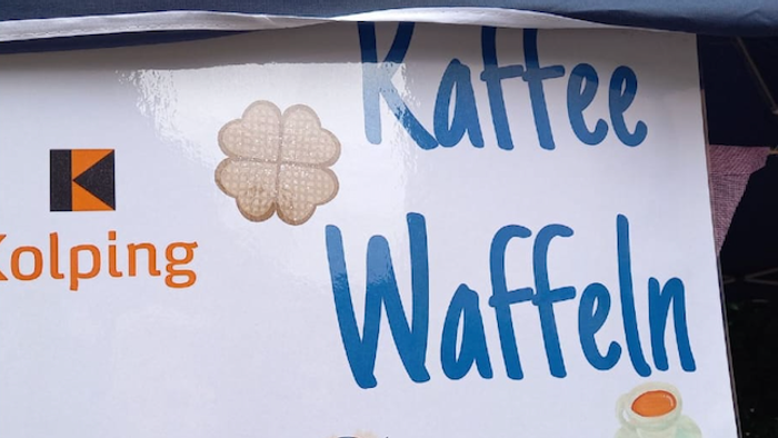 Ein Schild, das Kolpings Angebot von Kaffee und Waffeln auf einem Kirchplatzfest bewirbt.