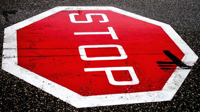 Stopschild-Zeichen, das auf eine Straße gemalt wurde. Leichte Fahrspuren sind zu sehen.