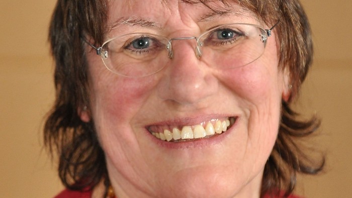 Eine Frau mit Brille und Perlenkette lächelt.