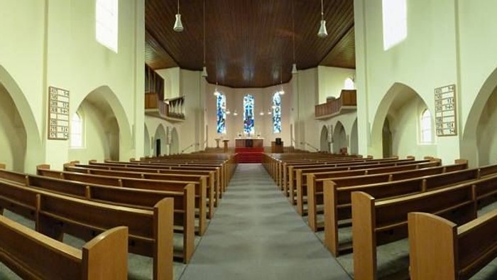 Leere Kirchenbankreihen vor Altar in heller Kirche