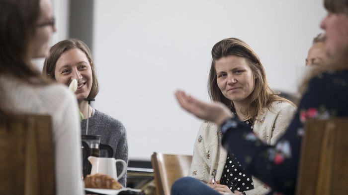 En gruppe kvinder sidder og snakker ved et bord med kaffe.
