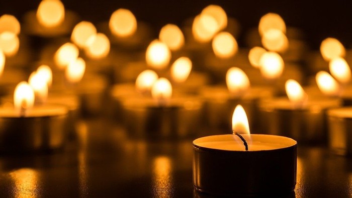 A close-up of a lit candle surrounded by many other lit candles in the background.