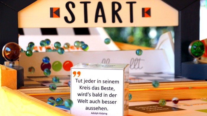 Ein Holz-Kugellaufspiel mit einem motivierenden Zitat auf Deutsch und bunten Murmeln.