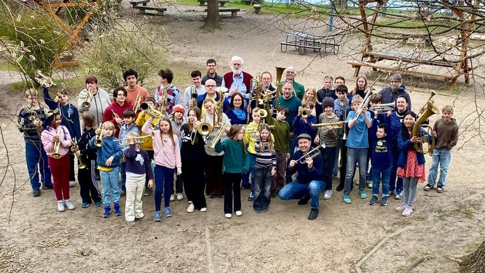 Eine große Gruppe von Menschen, darunter Kinder und Erwachsene, die sich gemeinsam im Freien in einer parkähnlichen Umgebung fotografieren lassen.