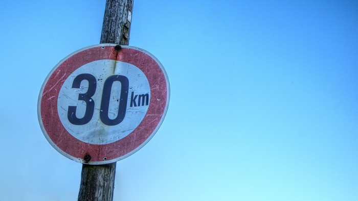 Ein verwittertes, rundes Geschwindigkeitsbegrenzungsschild mit 30 Kilometern pro Stunde vor einem klaren Himmel.