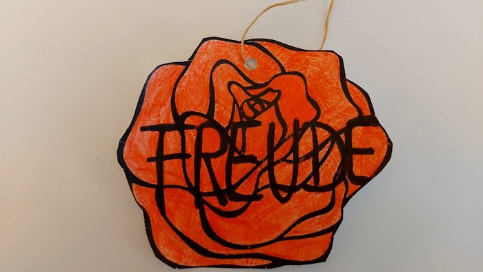 Handgefertigter Papieranhänger in Rosenform mit dem stilisierten Namen „Freddie“ darin.