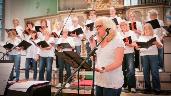 Eine Sängerin singt solo vor einem gemischten Chor in weißen Oberteilen in einer Kirche