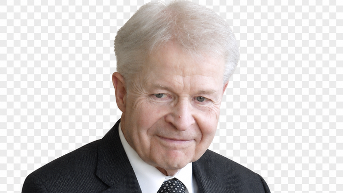 Eleganter älterer Herr im dunklen Anzug, weißem Hemd und gemusterten Krawatte, professionell posierend.