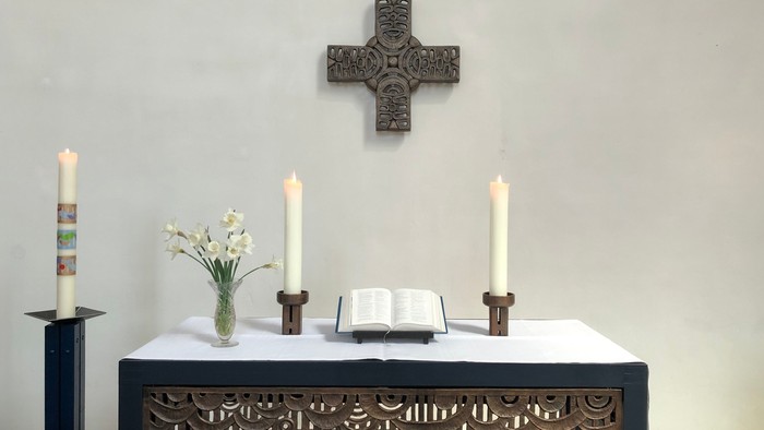 Ein Altar mit Kerzen, Blumen und einem Buch vor einem Kreuz an der Wand