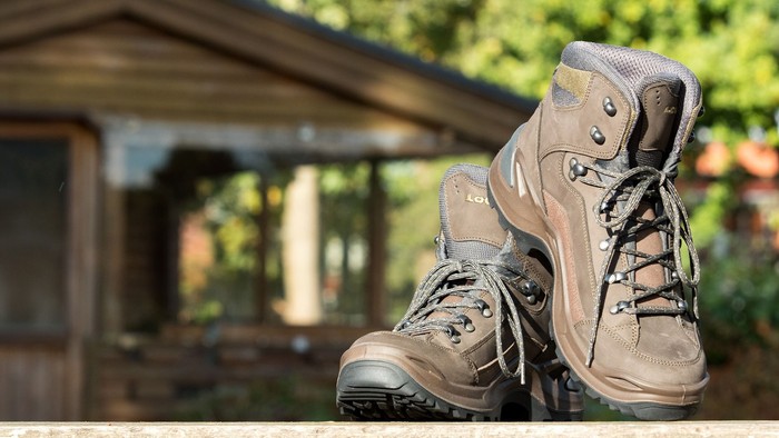 Die braunen Wanderstiefel stehen vor einer Holzhütte im Wald.