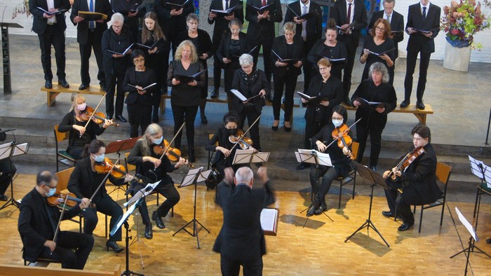Ein Chor und Kammerorchester, schwarz gekleidet, in einer modernen Kirche, von der Empore gesehen
