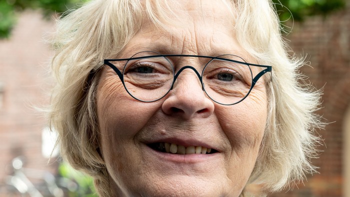 Eine etwa 60 Jahre alte Frau mit blonden, halblangen Haaren und einer schwarzen Brille schaut direkt in die Kamera.