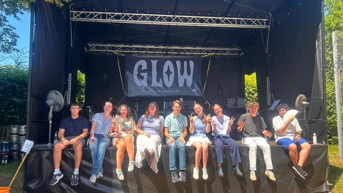 Eine Gruppe von Menschen posiert auf einer Bühne bei einer Open-Air-Veranstaltung mit dem Titel „GLOW“.
