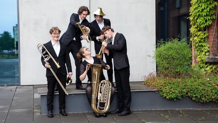 Eine Gruppe von Musiker:innen in formeller Kleidung, die im Freien mit verschiedenen Blechblasinstrumenten posieren.