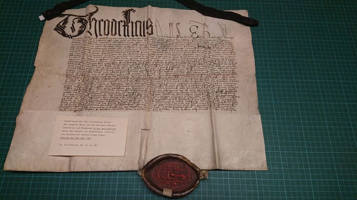 Historisches Pergamentdokument mit Wachssiegel und begleitender Informationskarte, wahrscheinlich eine königliche Urkunde oder ein Grundstücksbrief.