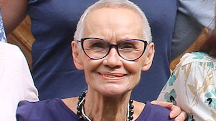 Eine ältere Frau mit Brille und einer Halskette, die lächelt.