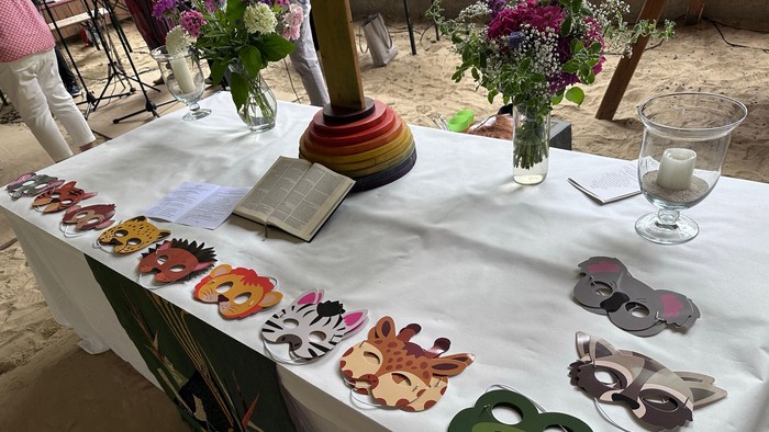 Bunte tiermotivierte Masken und ein geschmückter Tisch mit Blumen und Kerzen bei einer Outdoor-Veranstaltung.