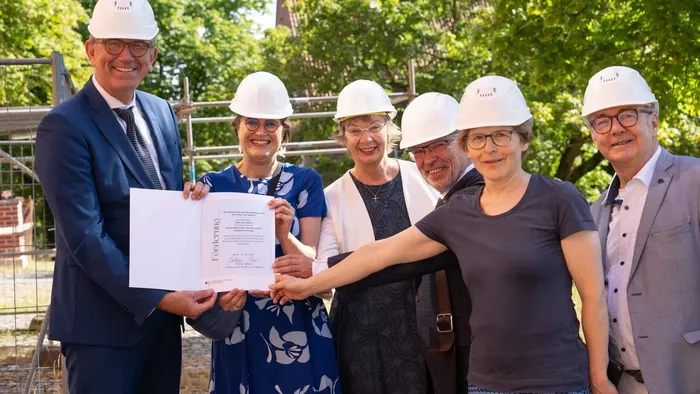 Frauen und Männer halten einen Förderbescheid in die Kamera - am Dom zu Lübeck.