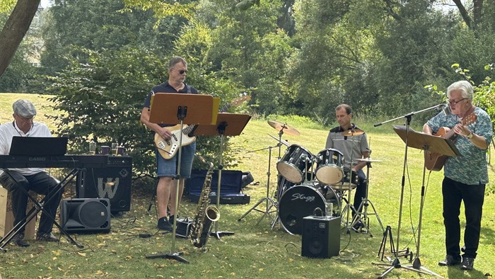 Eine Musikergruppe im grünen mit Keybord, Bass, Schlagzeug, Gitarre und Saxophon