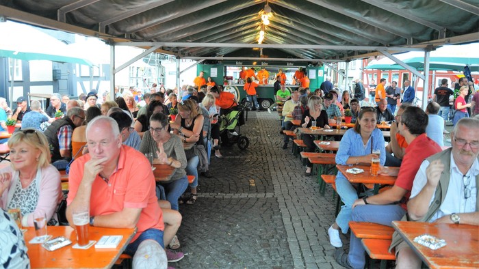 Belebter Außenbereich mit Gästen, die unter einem überdachten Pavillon Mahlzeiten und Getränke genießen.