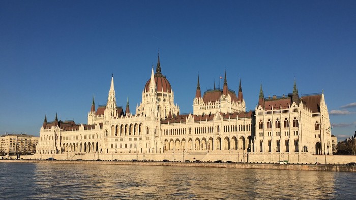 Großes, verziertes Gebäude am Flussufer bei klarem Himmel
