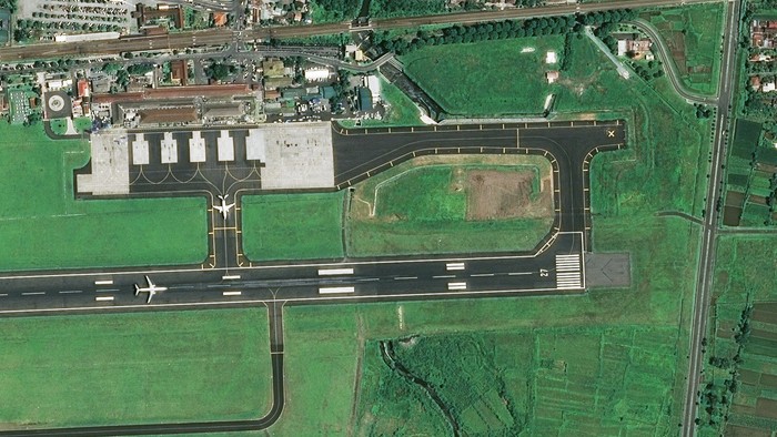 Aerial view of airport surrounded by urban area with green fields and buildings.