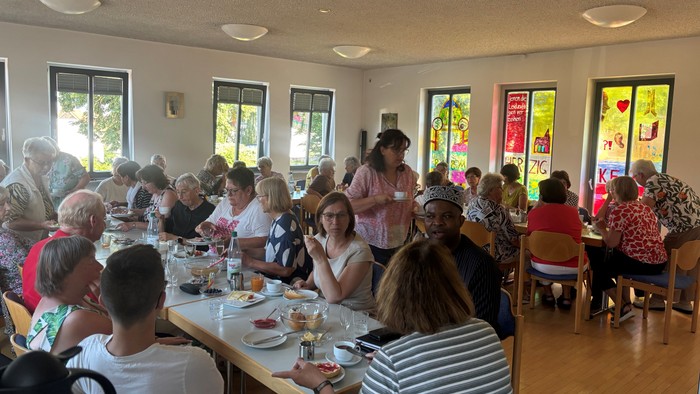 Gruppe von Menschen, die gemeinsam in einem hellen, geräumigen Innenraum mit Tischen voller Essen speisen.