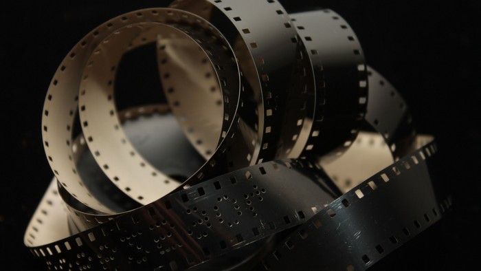 Gestapelte Filmrollen mit perforierten Rändern vor dunklem Hintergrund.