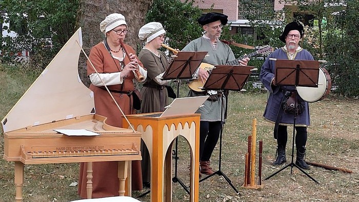 Historische Musiker in historischen Kostümen, die im Freien mit Instrumenten wie Cembalo, Blockflöte und Trommeln auftreten.
