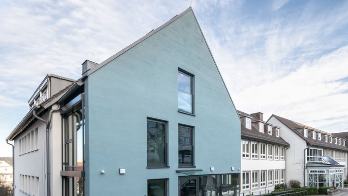 Modernes Gebäude mit hellblauer Fassade und Glaseingang neben einem Wohnkomplex.