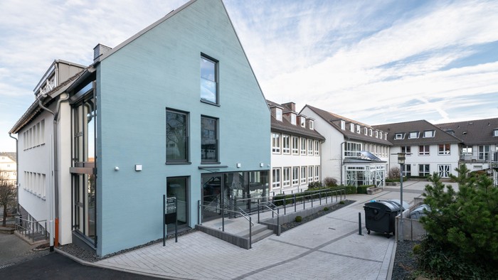 Modernes Gebäude mit hellblauer Fassade und Glaseingang neben einem Wohnkomplex.
