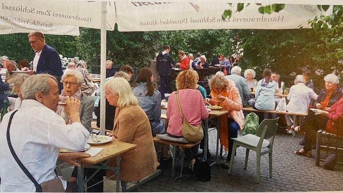 Freiluftcafé voller Menschen, die unter großen Sonnenschirmen Mahlzeiten genießen und sich unterhalten.