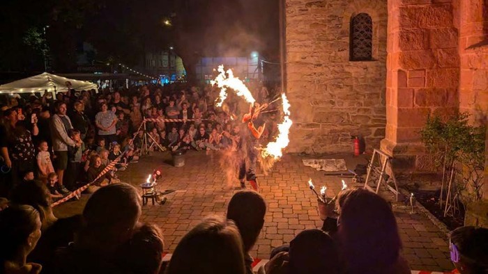Eine Person führt bei Nacht eine Feuerschaukel vor, umgeben von Zuschauern.