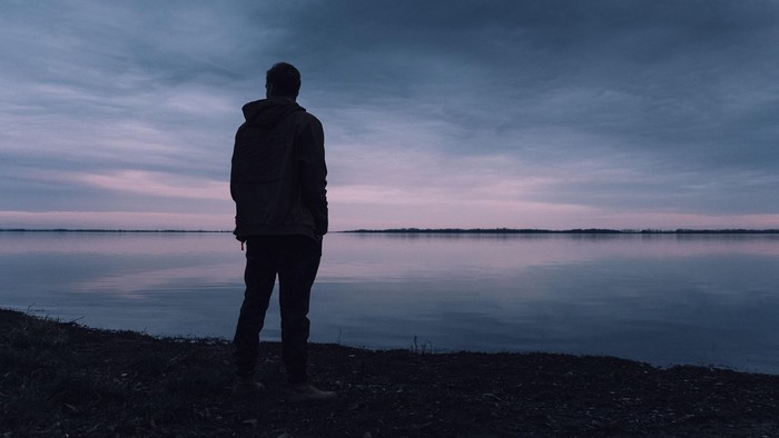 Mann steht am Ufer und schaut auf das Abendrot