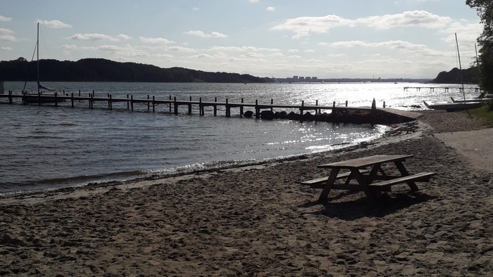 Ansicht von einem Sandstrand. Ein Holzsteg führt in die Ostsee. Auf dem Strand ein Campingtisch.